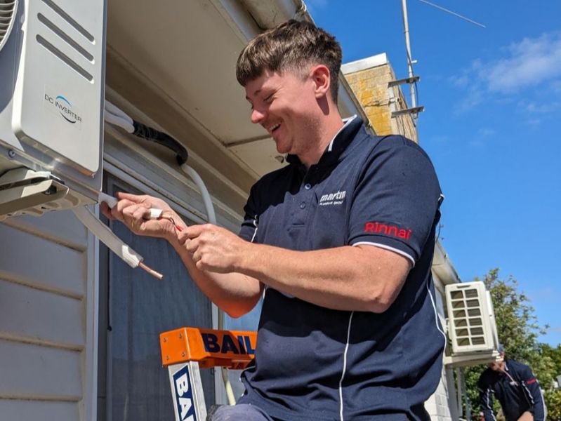 Technician installing an AC outdoor unit on a wall bracket